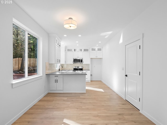 kitchen with appliances with stainless steel finishes, a peninsula, a sink, white cabinets, and light wood-type flooring