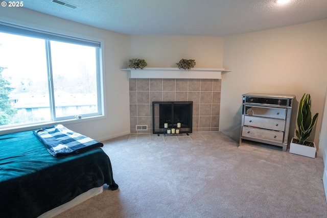 bedroom featuring a tile fireplace, light colored carpet, and a textured ceiling