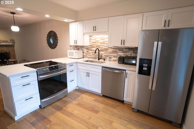 kitchen with sink, white cabinetry, decorative light fixtures, light hardwood / wood-style flooring, and appliances with stainless steel finishes