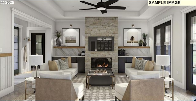 living room with ornamental molding, a tray ceiling, a stone fireplace, and light parquet floors