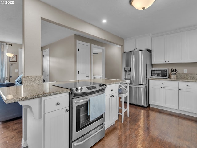 426 NE Hill St, Sheridan, OR 97378 - kitchen with appliances with stainless steel finishes, a kitchen breakfast bar, white cabinetry, dark wood-style flooring, and light stone counters