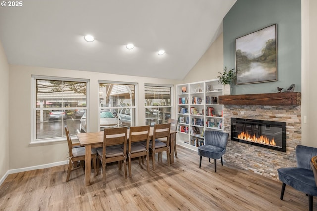 dining space with a fireplace, vaulted ceiling, and light hardwood / wood-style flooring