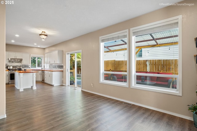 kitchen with butcher block countertops, appliances with stainless steel finishes, white cabinetry, wood-type flooring, and decorative backsplash