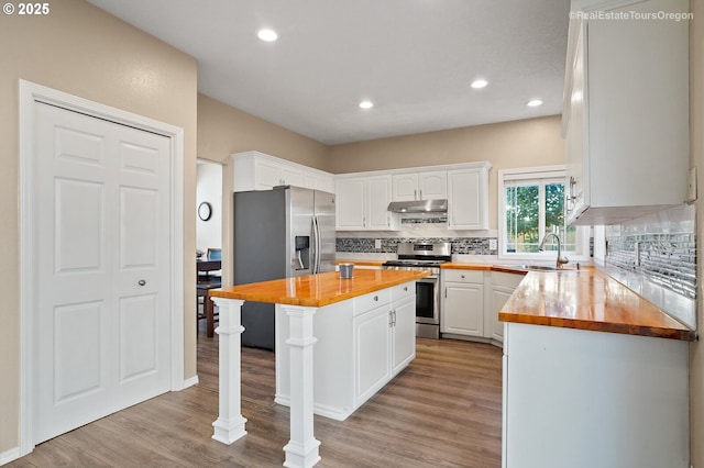 kitchen with stainless steel appliances, a center island, white cabinets, and butcher block countertops