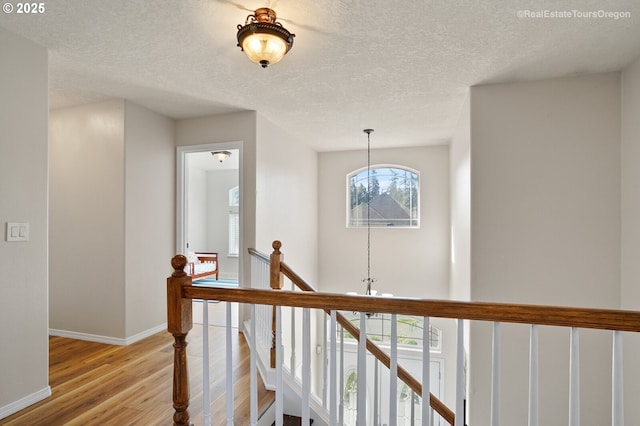 hallway featuring light hardwood / wood-style floors, a textured ceiling, and a notable chandelier