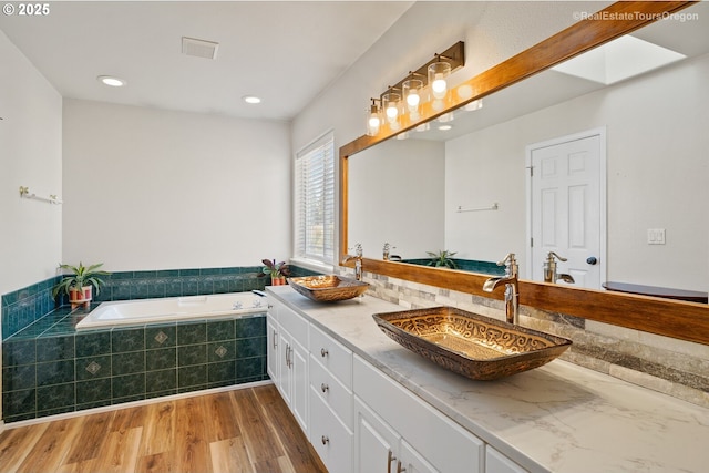 bathroom featuring vanity, hardwood / wood-style floors, a skylight, and tiled tub