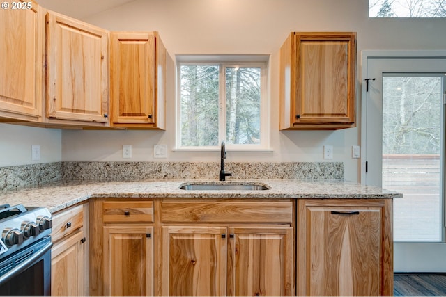 kitchen featuring light brown cabinets, stainless steel gas range, a sink, and light stone countertops