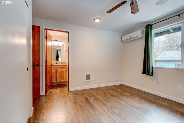 unfurnished bedroom with baseboards, a wall unit AC, ensuite bath, and light wood-style floors