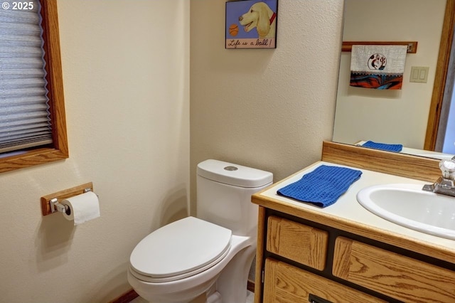 half bathroom with a textured wall, vanity, and toilet