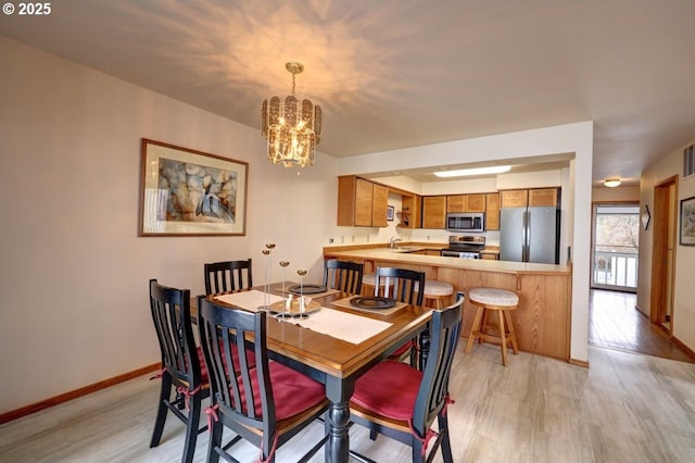 dining space with a chandelier, light wood-style floors, and baseboards