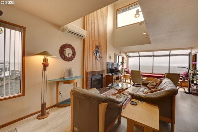 living room featuring a brick fireplace, a wall unit AC, baseboards, and wood finished floors