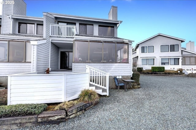 view of front of property featuring a sunroom, a balcony, and a chimney