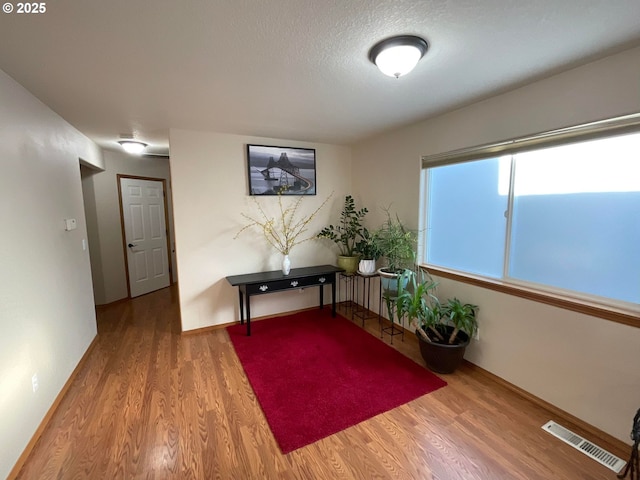 interior space featuring a textured ceiling, wood finished floors, baseboards, and visible vents