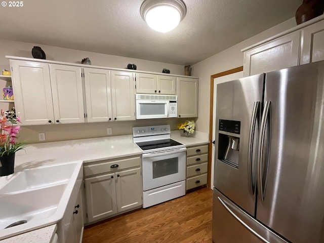 kitchen with white appliances, light wood-style flooring, light countertops, a textured ceiling, and a sink