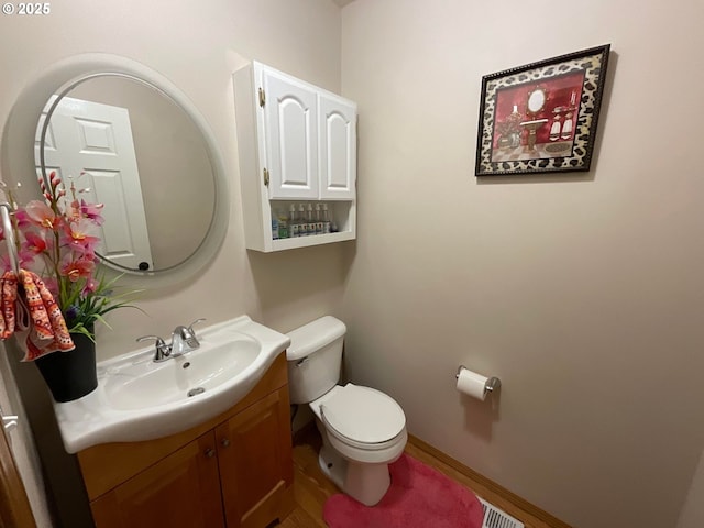half bath with visible vents, baseboards, toilet, vanity, and wood finished floors