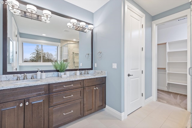 bathroom featuring a shower stall, double vanity, baseboards, and a sink