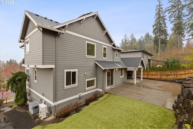 rear view of property with a yard, a patio area, fence, and a shingled roof