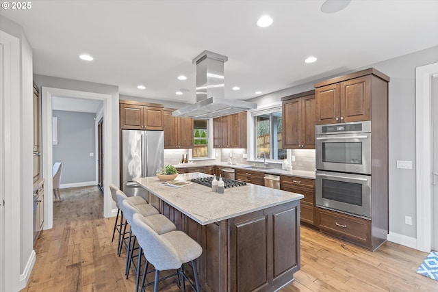 kitchen with stainless steel appliances, light wood-style floors, a kitchen breakfast bar, backsplash, and island range hood