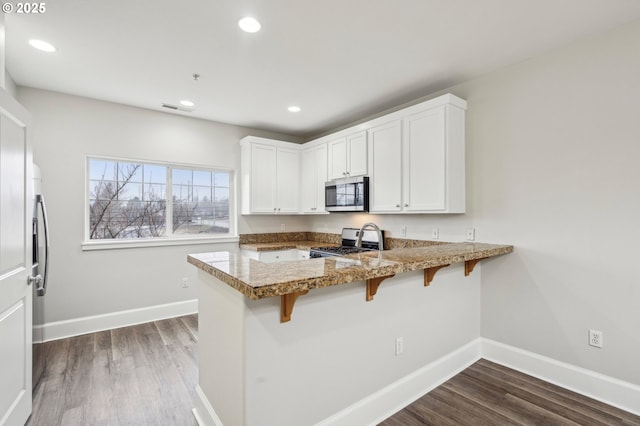 kitchen featuring appliances with stainless steel finishes, a breakfast bar area, light stone counters, white cabinets, and kitchen peninsula