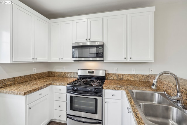 kitchen featuring white cabinets, stainless steel appliances, dark stone counters, and sink