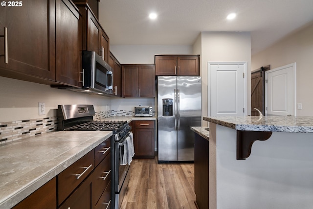 kitchen featuring stainless steel appliances, light hardwood / wood-style flooring, a breakfast bar area, a barn door, and dark brown cabinetry