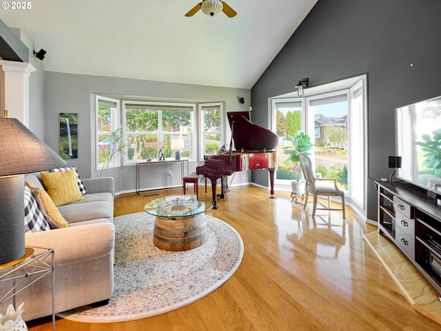 living area featuring light wood finished floors, baseboards, ceiling fan, ornate columns, and high vaulted ceiling