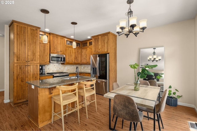 17760 SW Robert Ln, Beaverton, OR 97078 - kitchen featuring appliances with stainless steel finishes, a chandelier, decorative backsplash, dark stone countertops, and wood finished floors