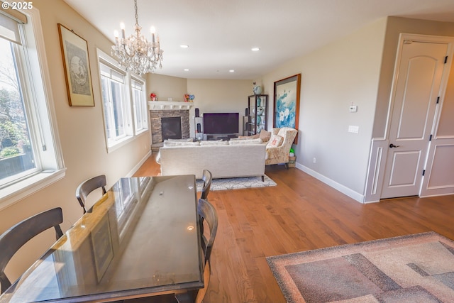 dining area with baseboards, wood finished floors, a stone fireplace, a notable chandelier, and recessed lighting