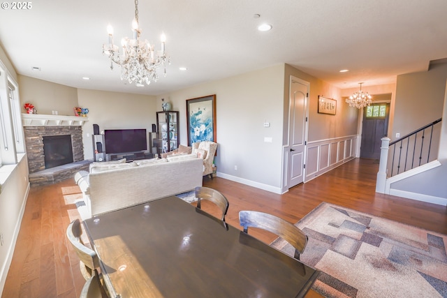 dining space featuring an inviting chandelier, a stone fireplace, wood finished floors, and recessed lighting