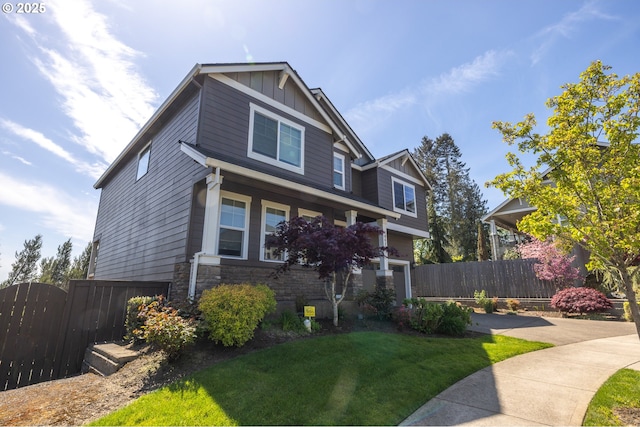 craftsman-style home with stone siding, board and batten siding, a front yard, and fence