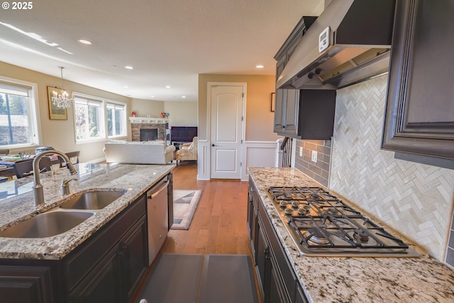 kitchen with under cabinet range hood, a fireplace, a sink, light wood-style floors, and appliances with stainless steel finishes