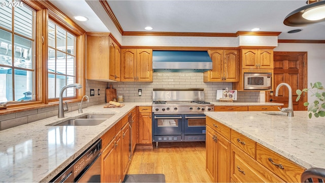 kitchen with sink, stainless steel appliances, wall chimney exhaust hood, and light stone countertops