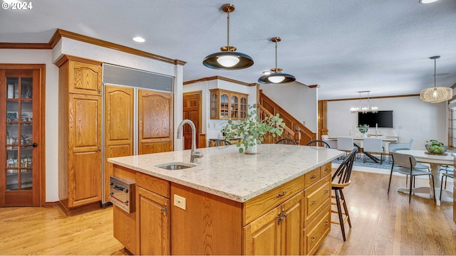 kitchen featuring pendant lighting, sink, crown molding, light hardwood / wood-style flooring, and a kitchen island with sink