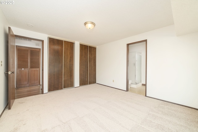 unfurnished bedroom with light carpet, a textured ceiling, multiple closets, and ensuite bathroom