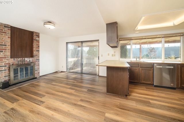 kitchen featuring sink, dishwasher, wood-type flooring, a fireplace, and kitchen peninsula