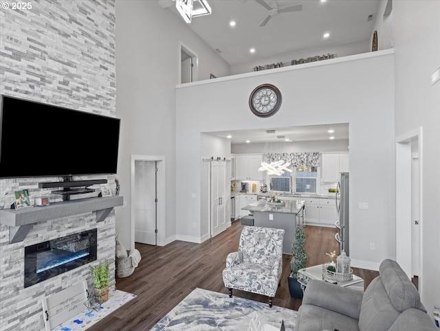 living room featuring ceiling fan, a stone fireplace, a towering ceiling, and dark hardwood / wood-style flooring