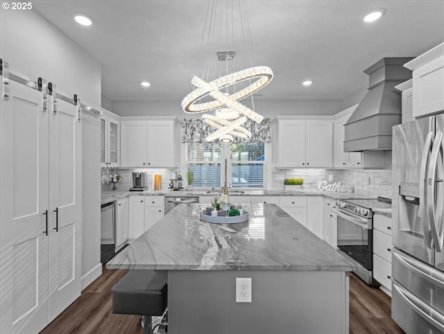 kitchen with a barn door, appliances with stainless steel finishes, a center island, and white cabinets