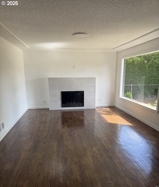 1640 Manor Dr, Gladstone, OR 97027 - unfurnished living room featuring dark wood-style floors, baseboards, a textured ceiling, and a tiled fireplace