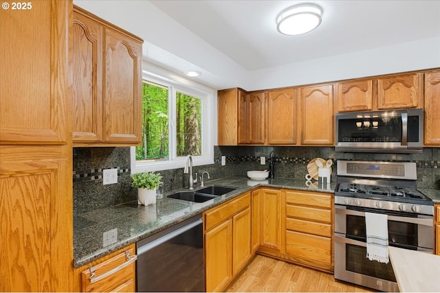 kitchen with dark stone countertops, a sink, light wood-type flooring, tasteful backsplash, and appliances with stainless steel finishes