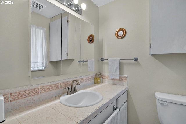 bathroom featuring toilet, visible vents, decorative backsplash, and vanity