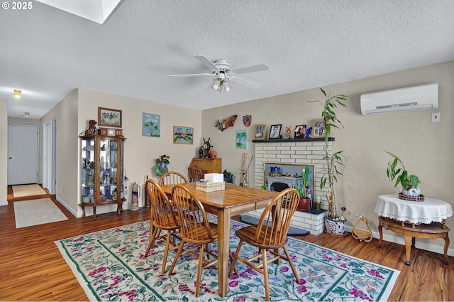 dining room featuring a brick fireplace, a textured ceiling, a ceiling fan, a wall unit AC, and wood finished floors