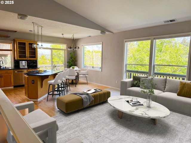 living room with visible vents, an inviting chandelier, light wood-style floors, baseboards, and vaulted ceiling