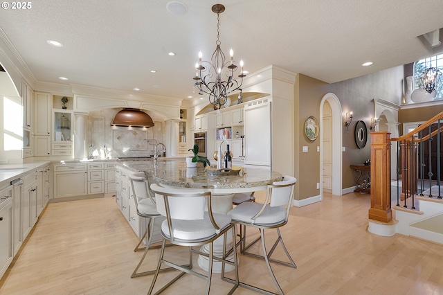 kitchen featuring pendant lighting, a breakfast bar, a spacious island, stainless steel oven, and light wood-type flooring