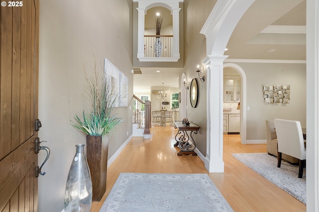 entrance foyer with decorative columns, ornamental molding, and light wood-type flooring