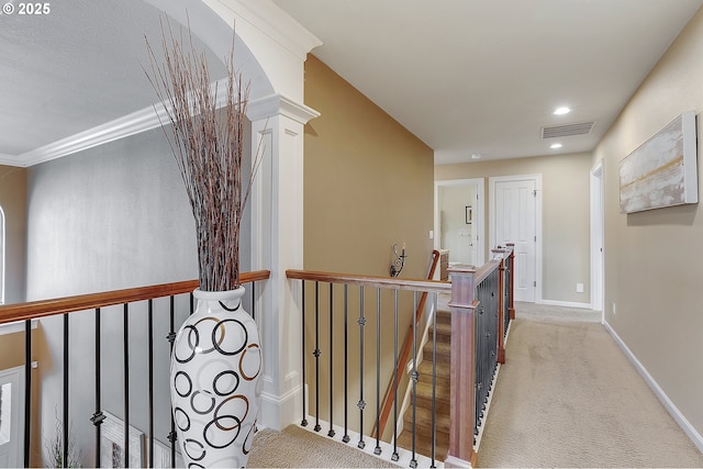 corridor with decorative columns, crown molding, and light colored carpet