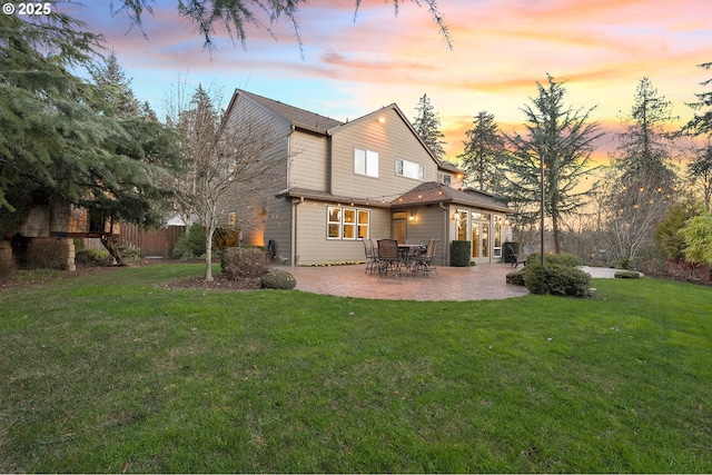 back house at dusk with a patio and a lawn