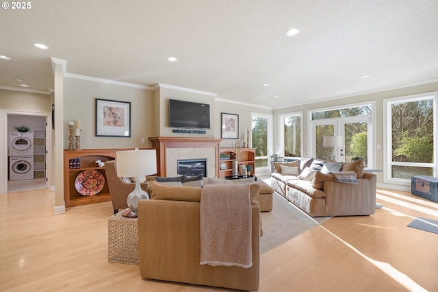 living room featuring stacked washer and dryer, a tiled fireplace, ornamental molding, and light hardwood / wood-style floors