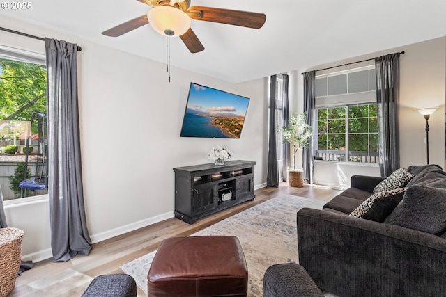 living area featuring healthy amount of natural light, wood finished floors, a ceiling fan, and baseboards