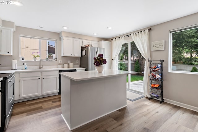 kitchen with a sink, stainless steel appliances, light countertops, white cabinets, and light wood-type flooring