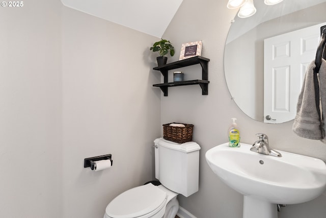 half bathroom with a sink, toilet, lofted ceiling, and baseboards